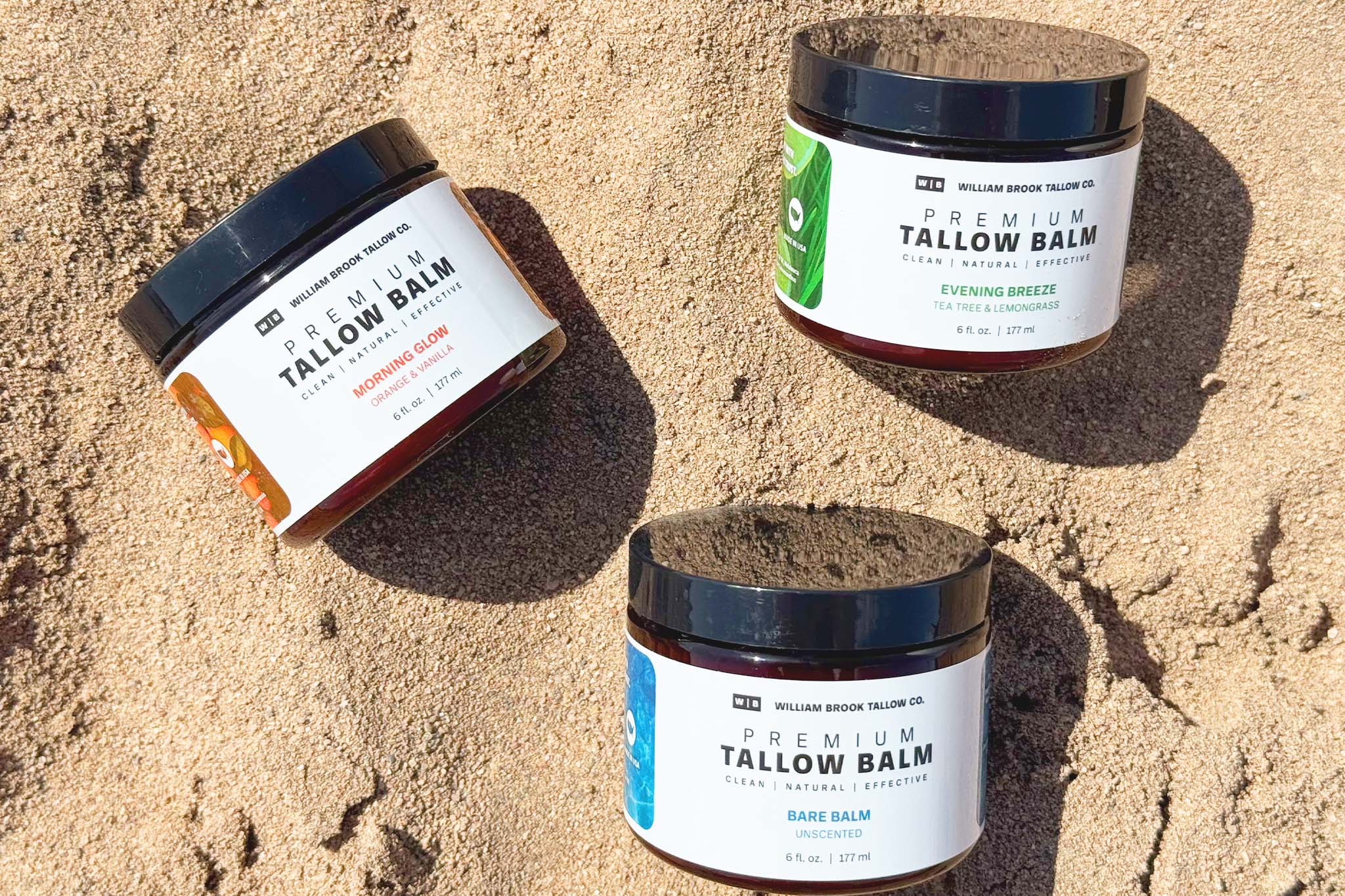 Three jars of tallow balm on a sandy surface
